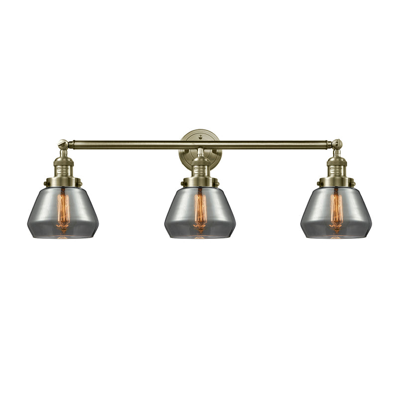 Fulton Bath Vanity Light shown in the Antique Brass finish with a Plated Smoke shade